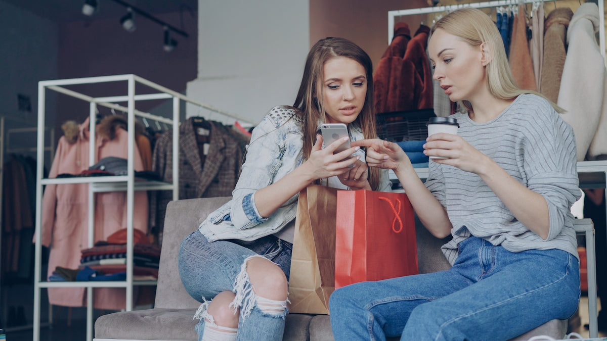 Two women are looking at a phone in a clothing store.